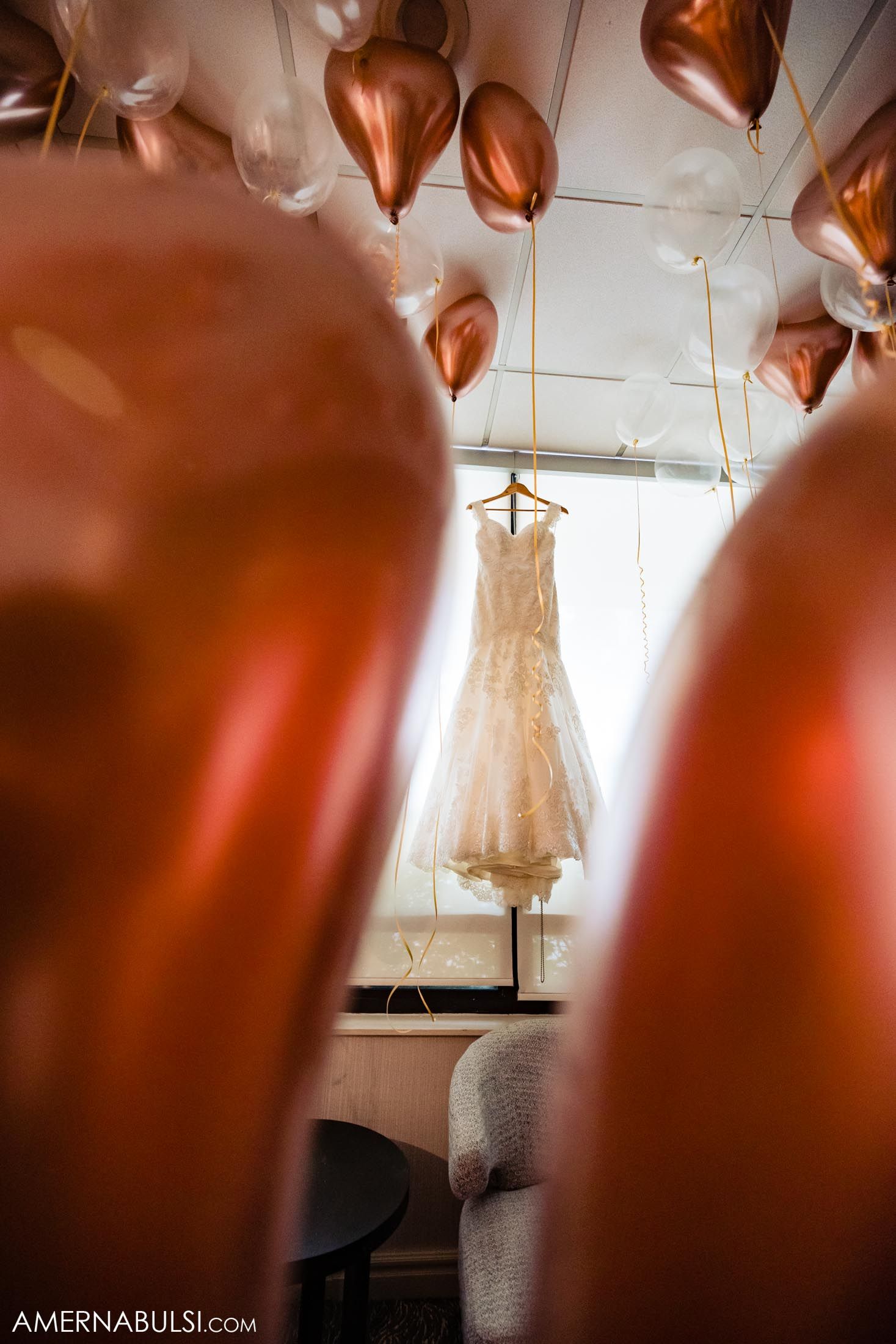 Wedding dress displayed among copper-colored balloons in an elegant setting.