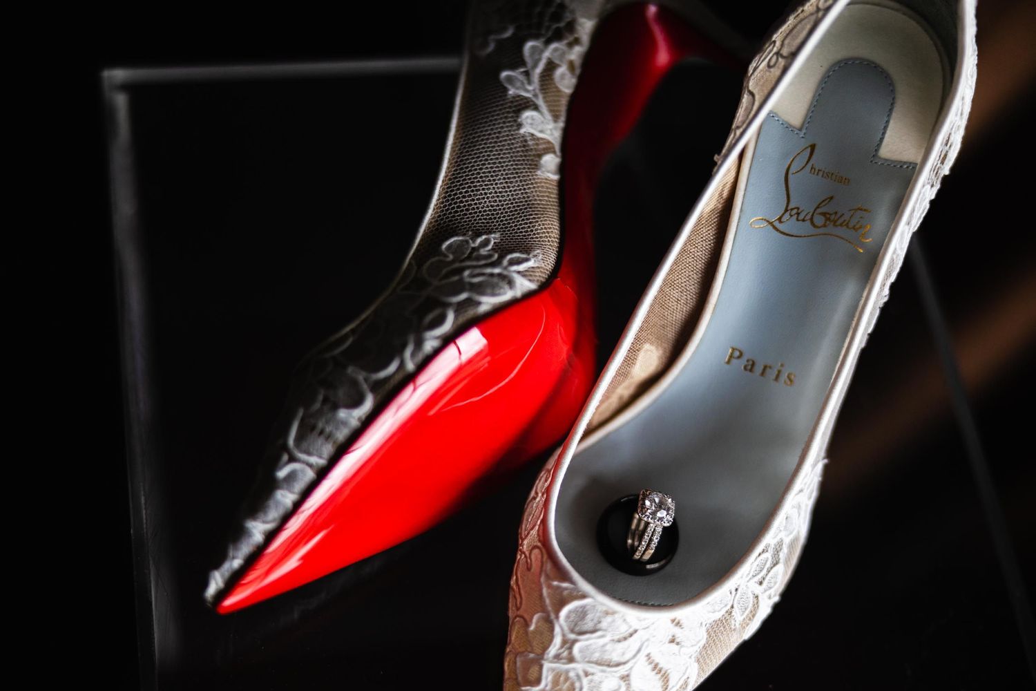 Elegant designer wedding shoes with lace detailing and red soles photographed against a dark background.