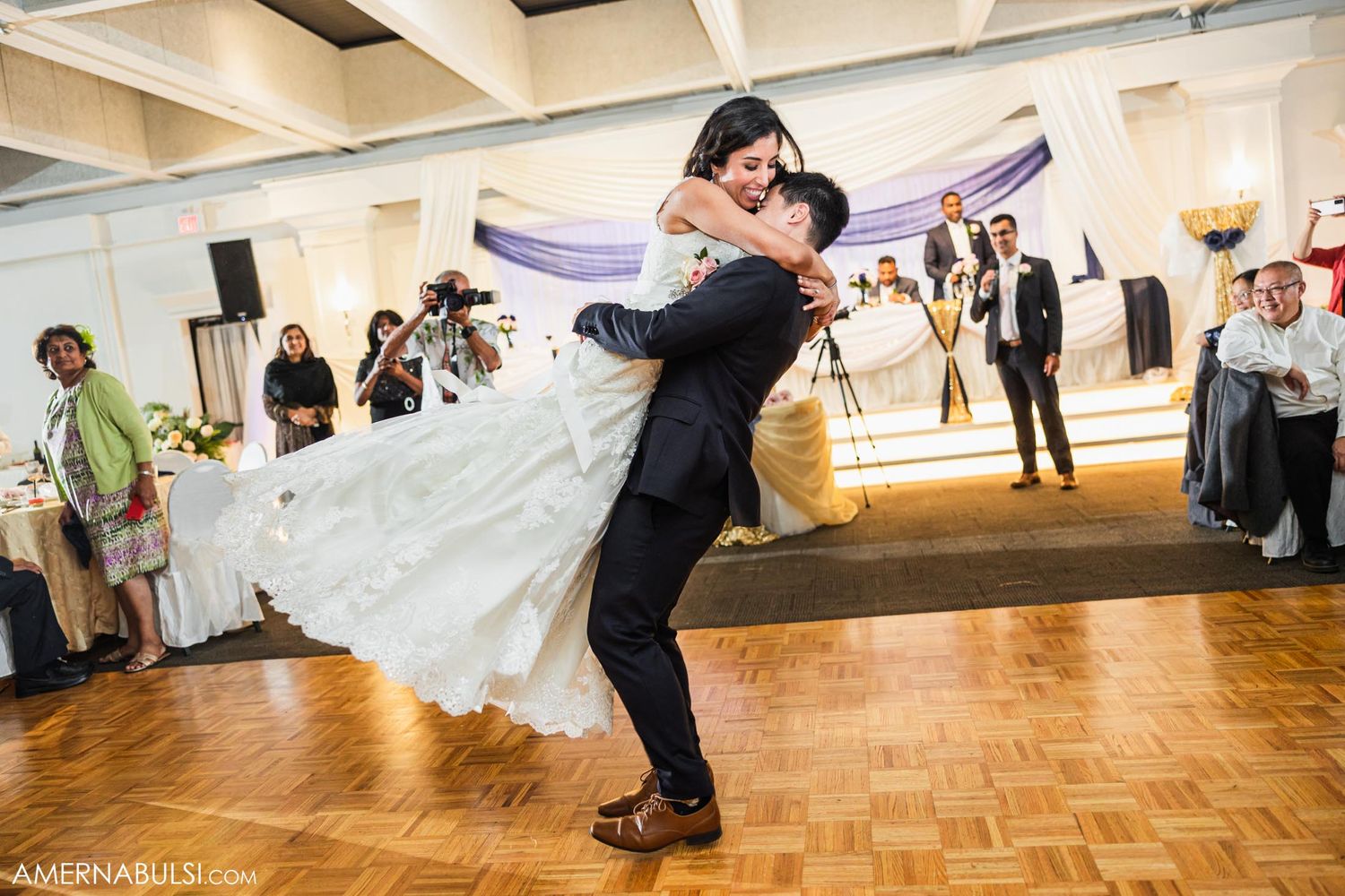 Romantic dance lift captured during a wedding reception on wooden parquet flooring.