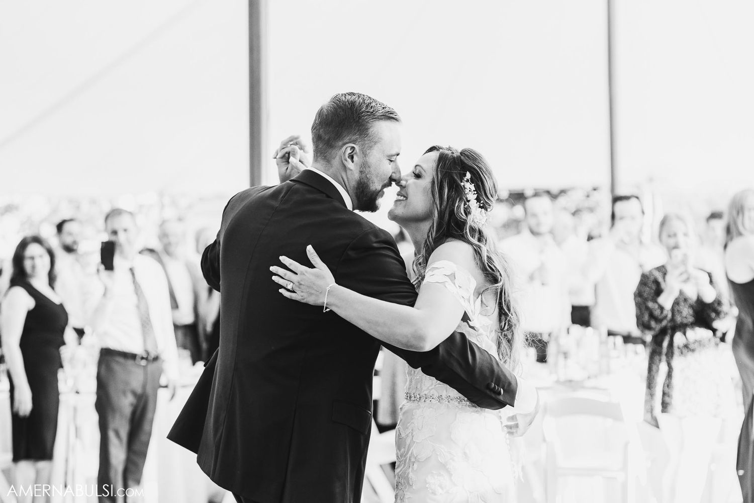 Intimate moment between newlyweds sharing their first dance at reception under white tent.