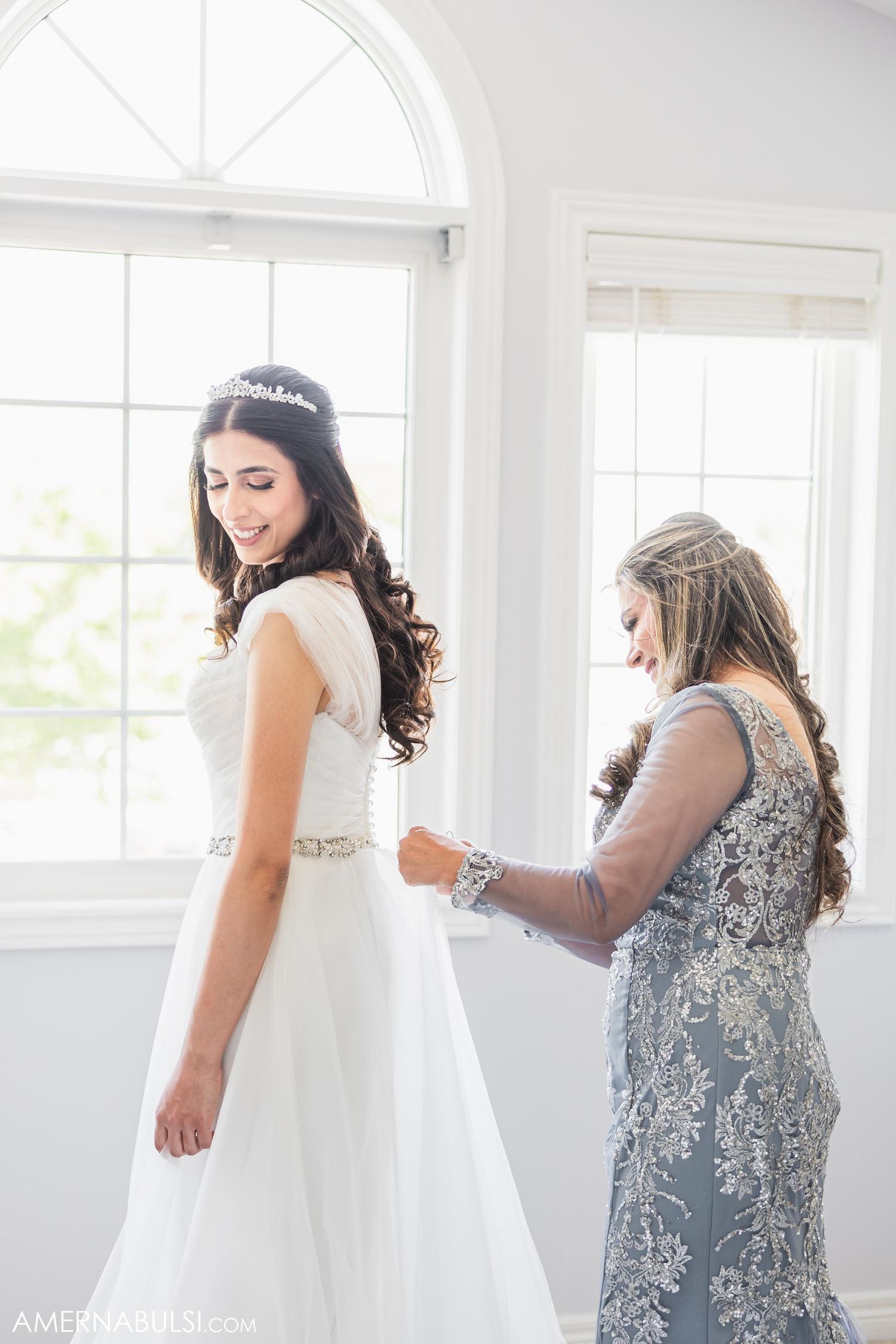Final dress adjustments being made as bride stands in natural window light.