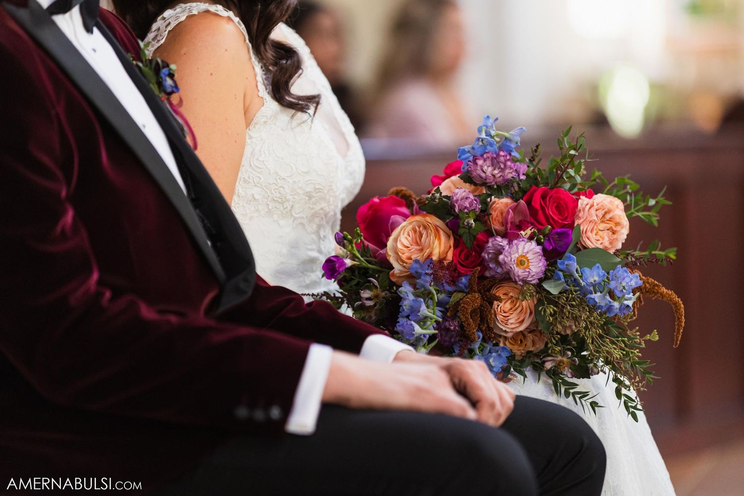 Colorful wedding bouquet with red, pink and blue flowers held during church ceremony.