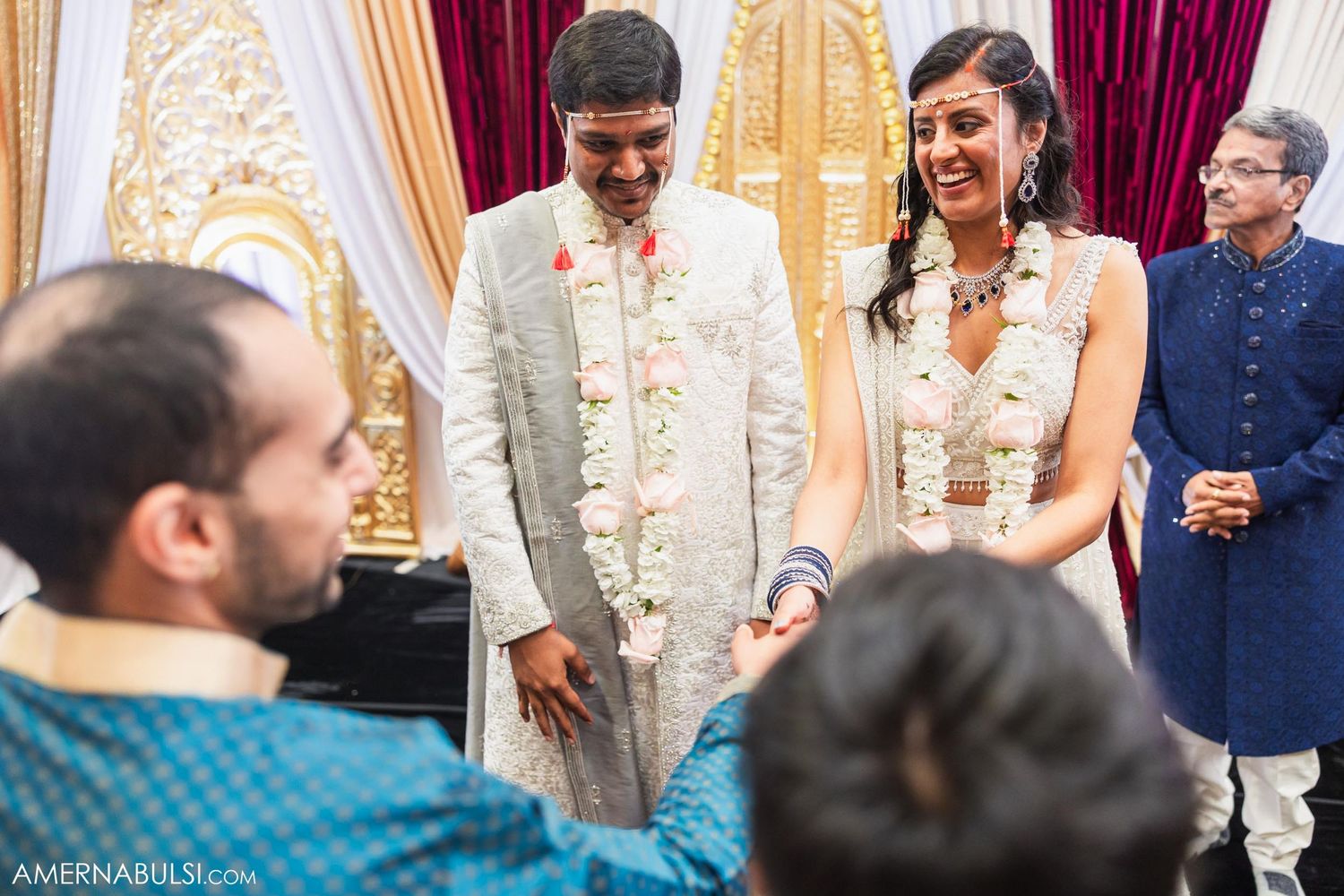 A couple participates in a traditional Indian wedding ceremony with guests watching.