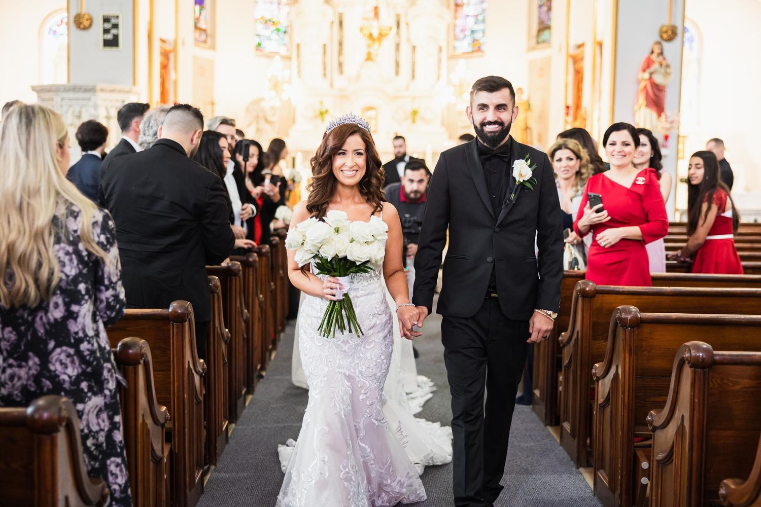 Wedding couple walks down church aisle while guests in pews look on.