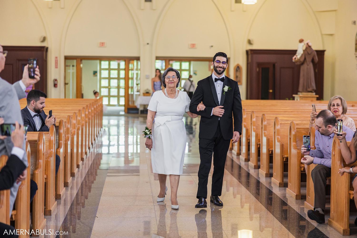 Wedding attendants walk down the center aisle of a church during a ceremony.