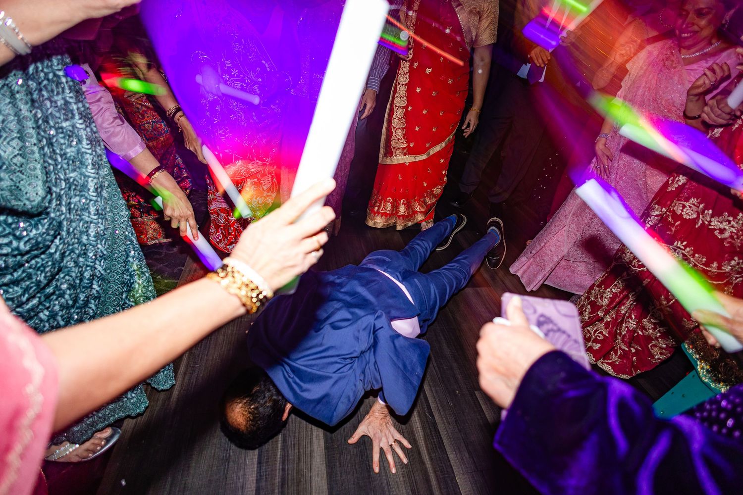 People dancing at a nightclub with vibrant purple lighting and colorful effects creating an energetic party atmosphere.