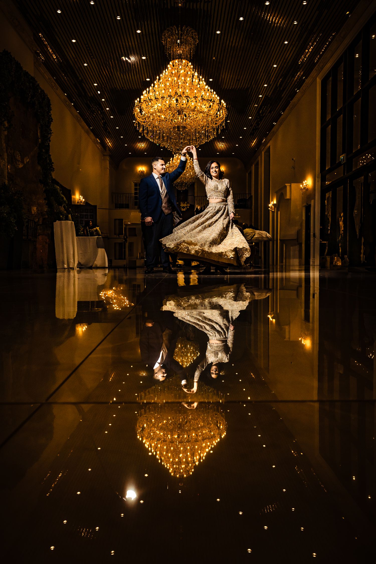 Dramatic chandelier reflections on polished ballroom floor creating mirror-like symmetry in dark lighting.