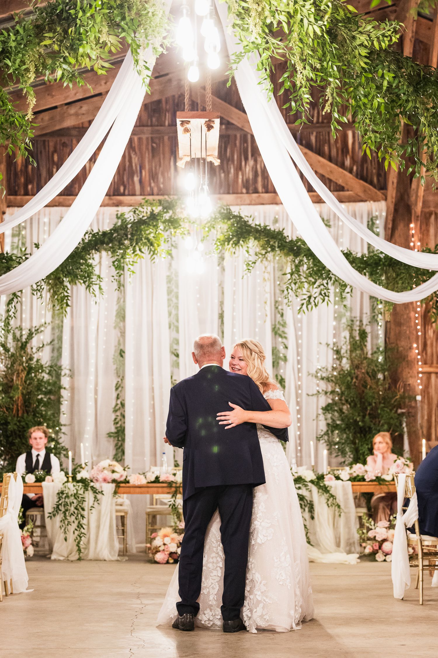 Romantic first dance moment under draped fabric and greenery in an elegantly decorated barn.