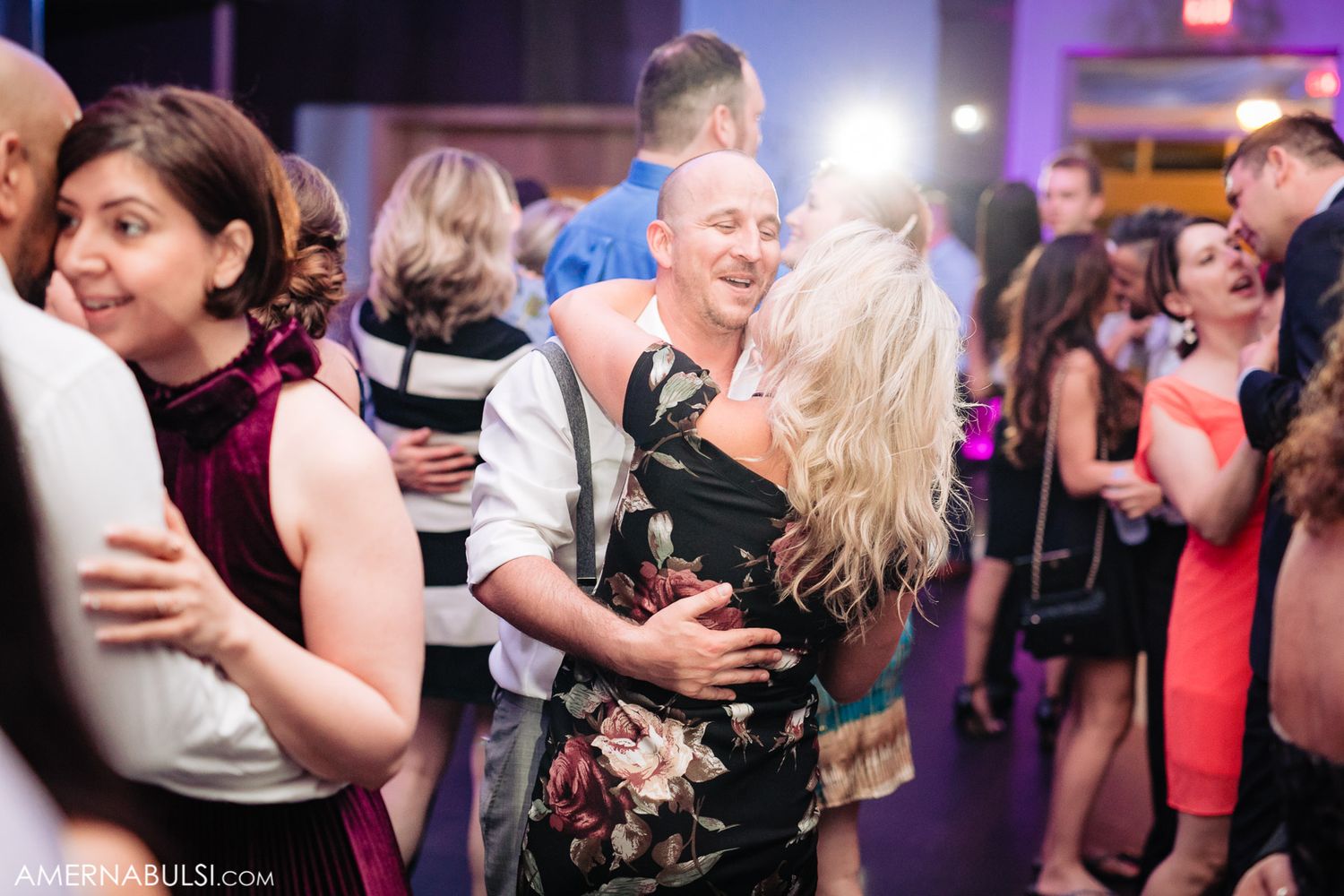 Couples dance closely together at a dimly lit wedding reception with purple ambient lighting.