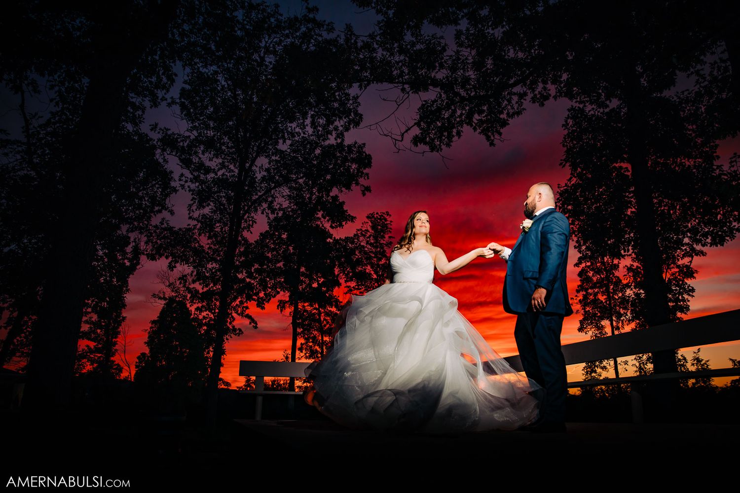 Dramatic sunset silhouettes a bride and groom against an orange and purple sky during their outdoor wedding photos.