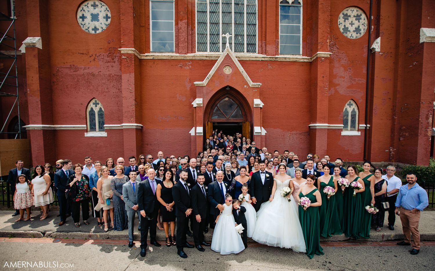 Large group wedding photo outside historic red brick church with entire wedding party.