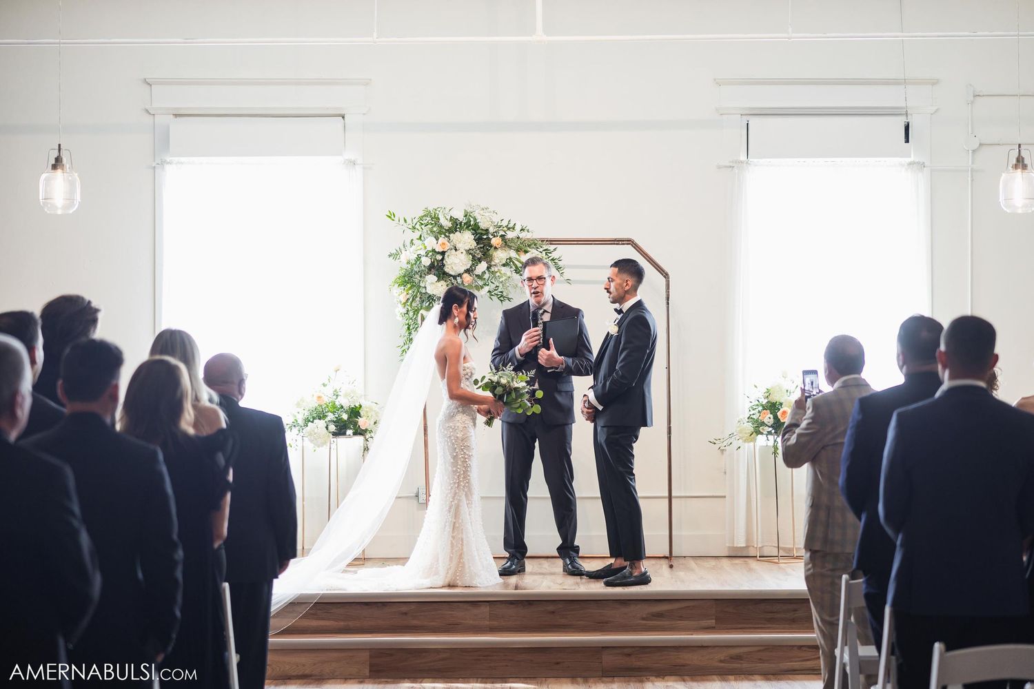 Wedding ceremony in a bright white venue with exposed brick walls and elegant floral arrangements.