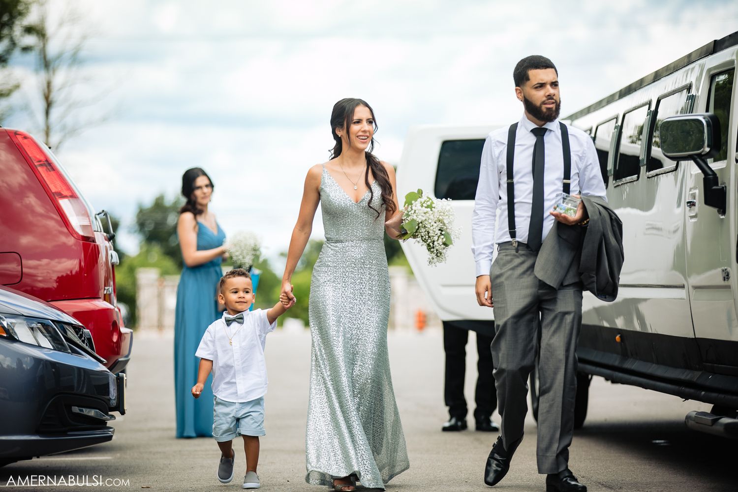 Wedding party members walking beside white limousines on an overcast day.