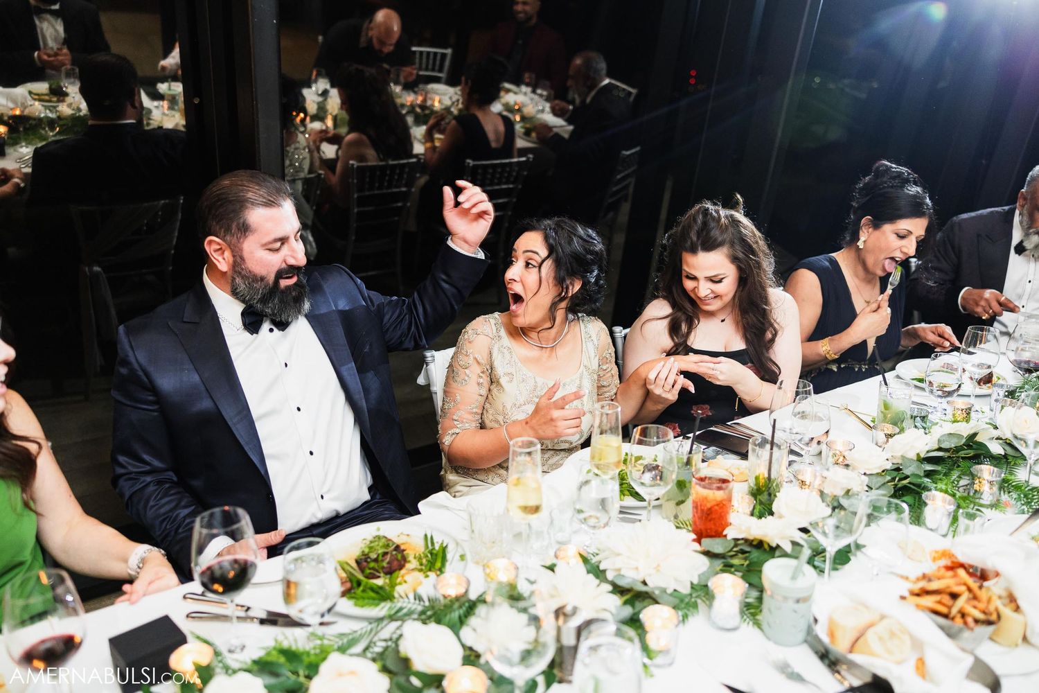 Wedding reception guests enjoying dinner at elegantly decorated table with floral centerpieces.