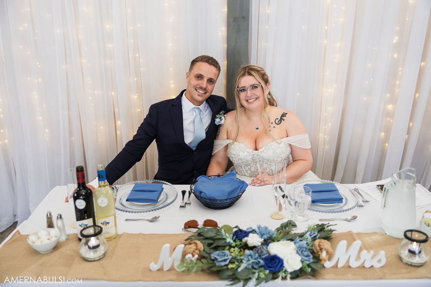 Wedding reception table decorated with greenery and 'Mr & Mrs' signs at elegant venue.