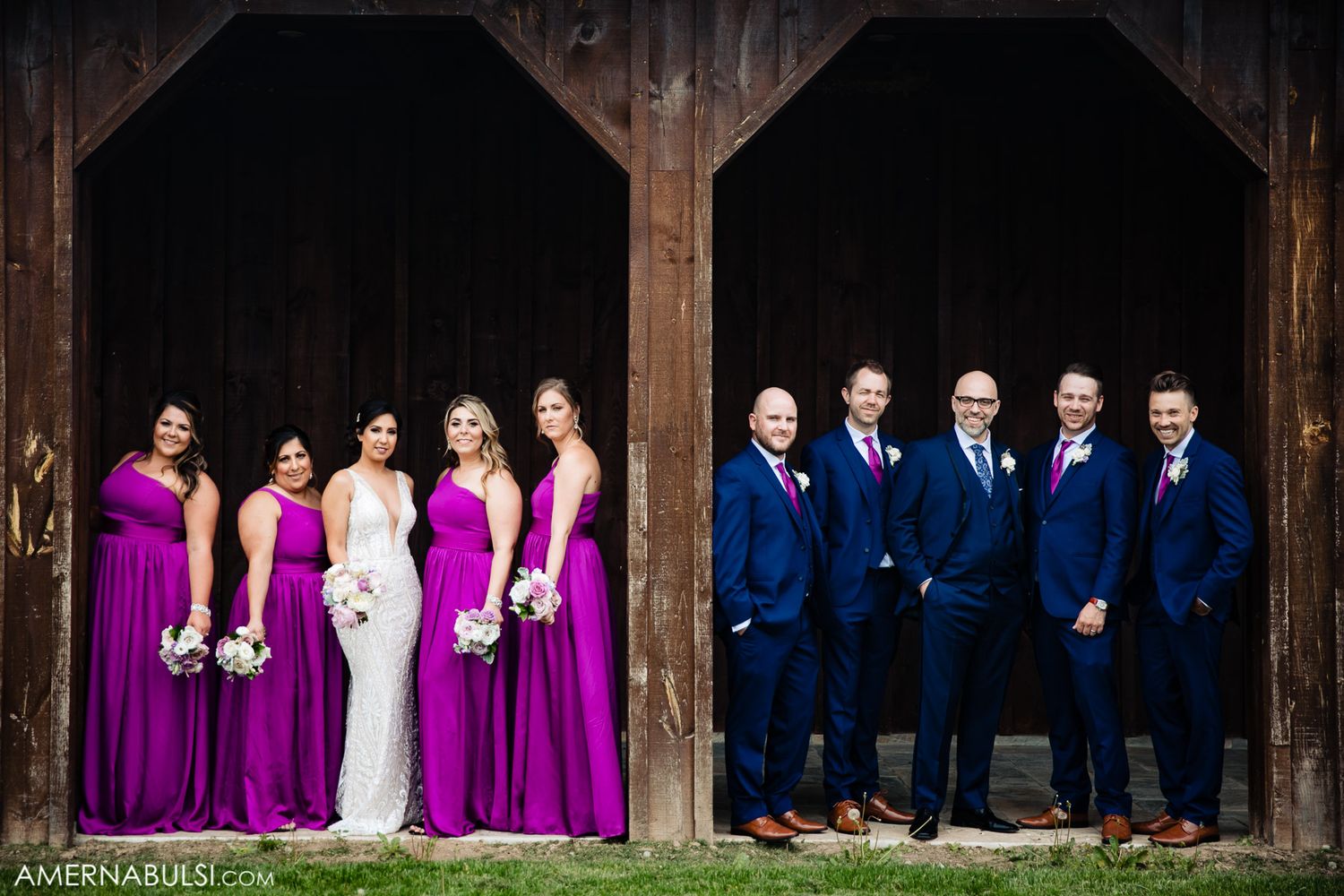 Wedding party posing in a rustic wooden pavilion wearing purple and navy attire.