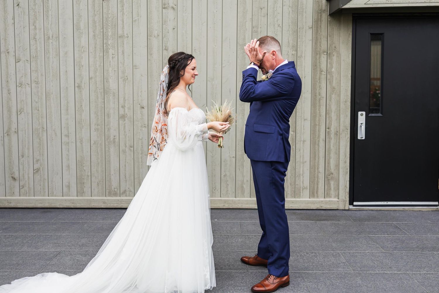 Emotional first look moment between couple against wooden wall backdrop.