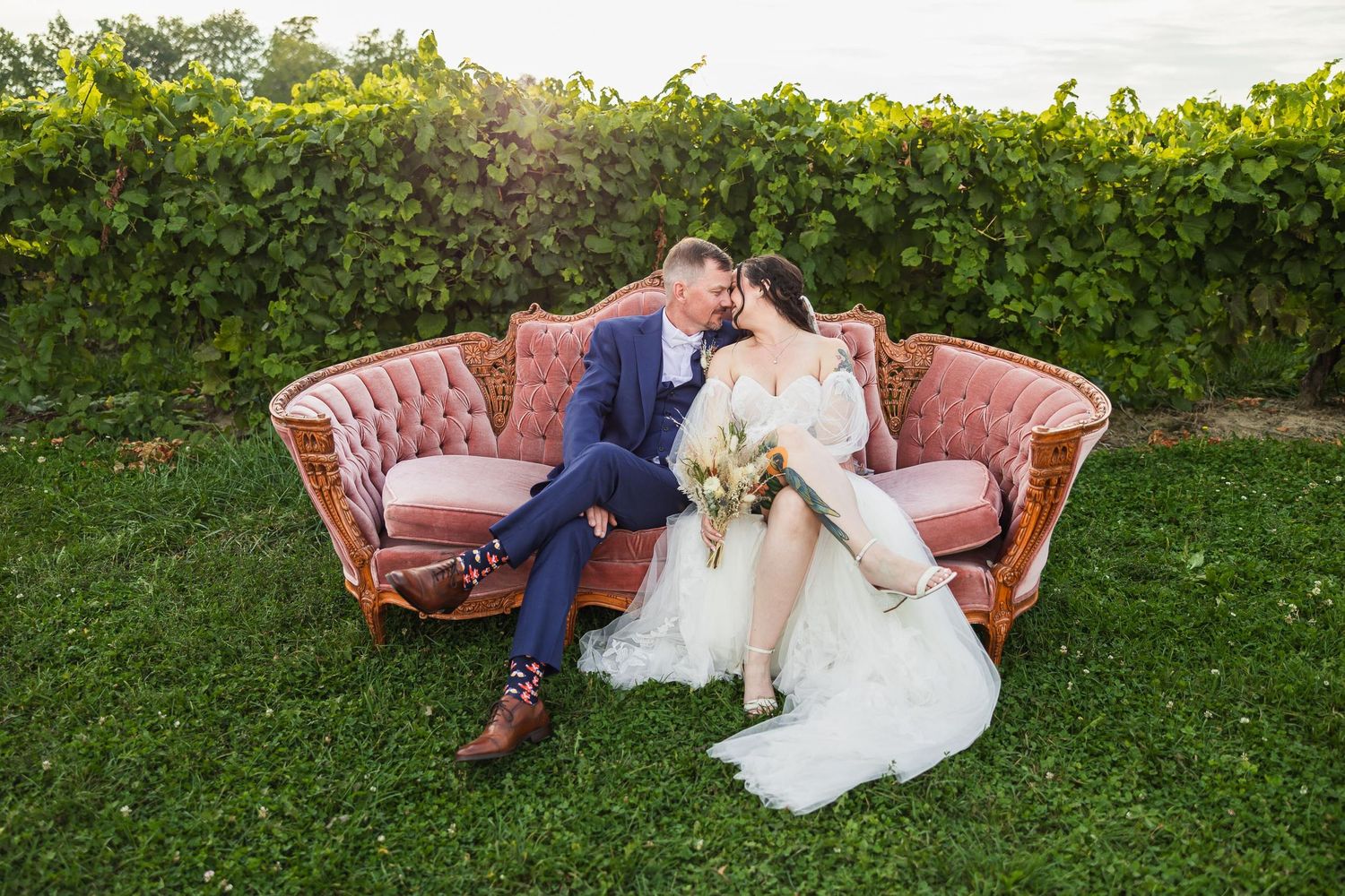 Couple sharing tender moment on pink vintage couch in garden setting.
