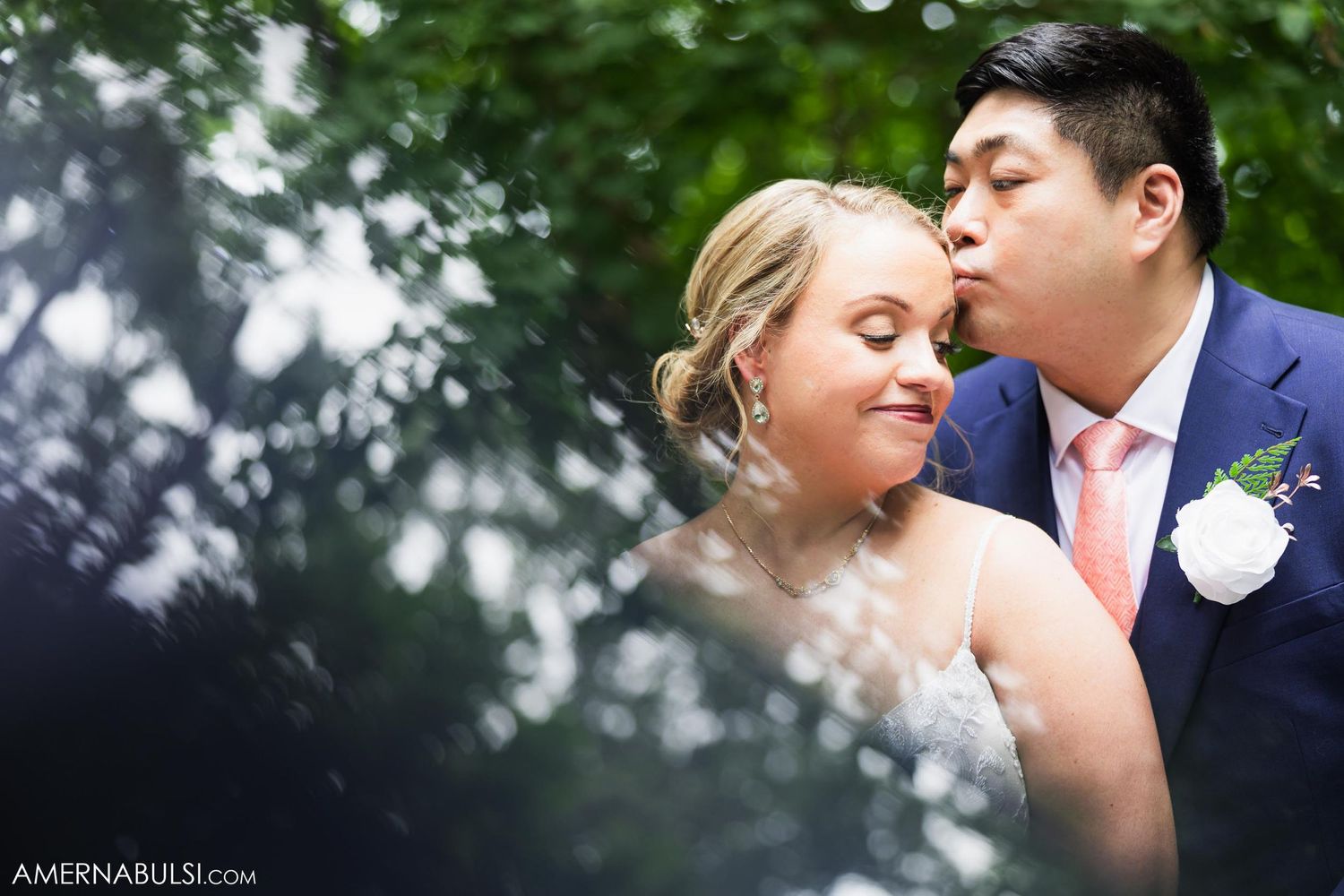 An intimate wedding portrait captured through soft greenery and natural lighting.
