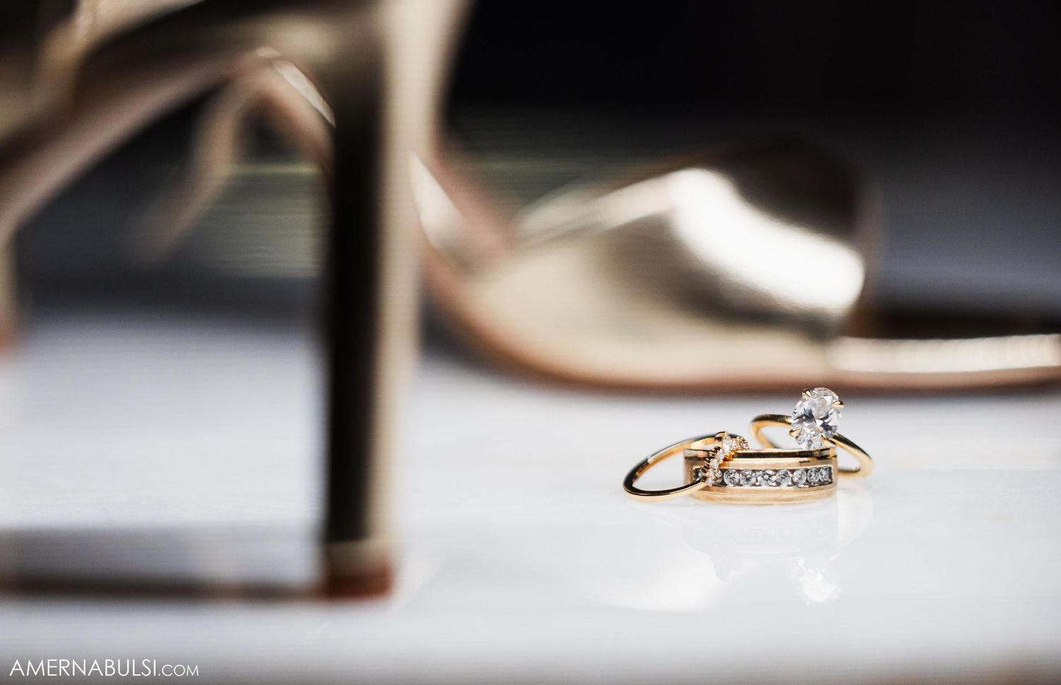 Close up of gold wedding rings and engagement ring next to high heel shoes.