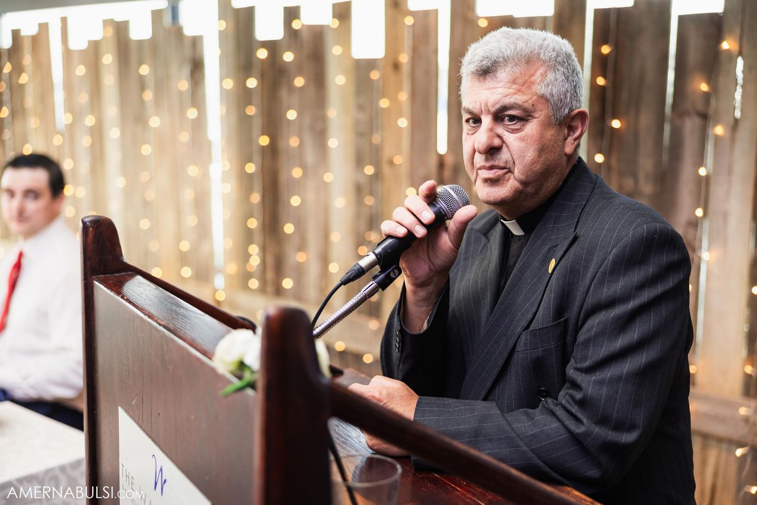 Speaker at a formal event using microphone with string lights in background.