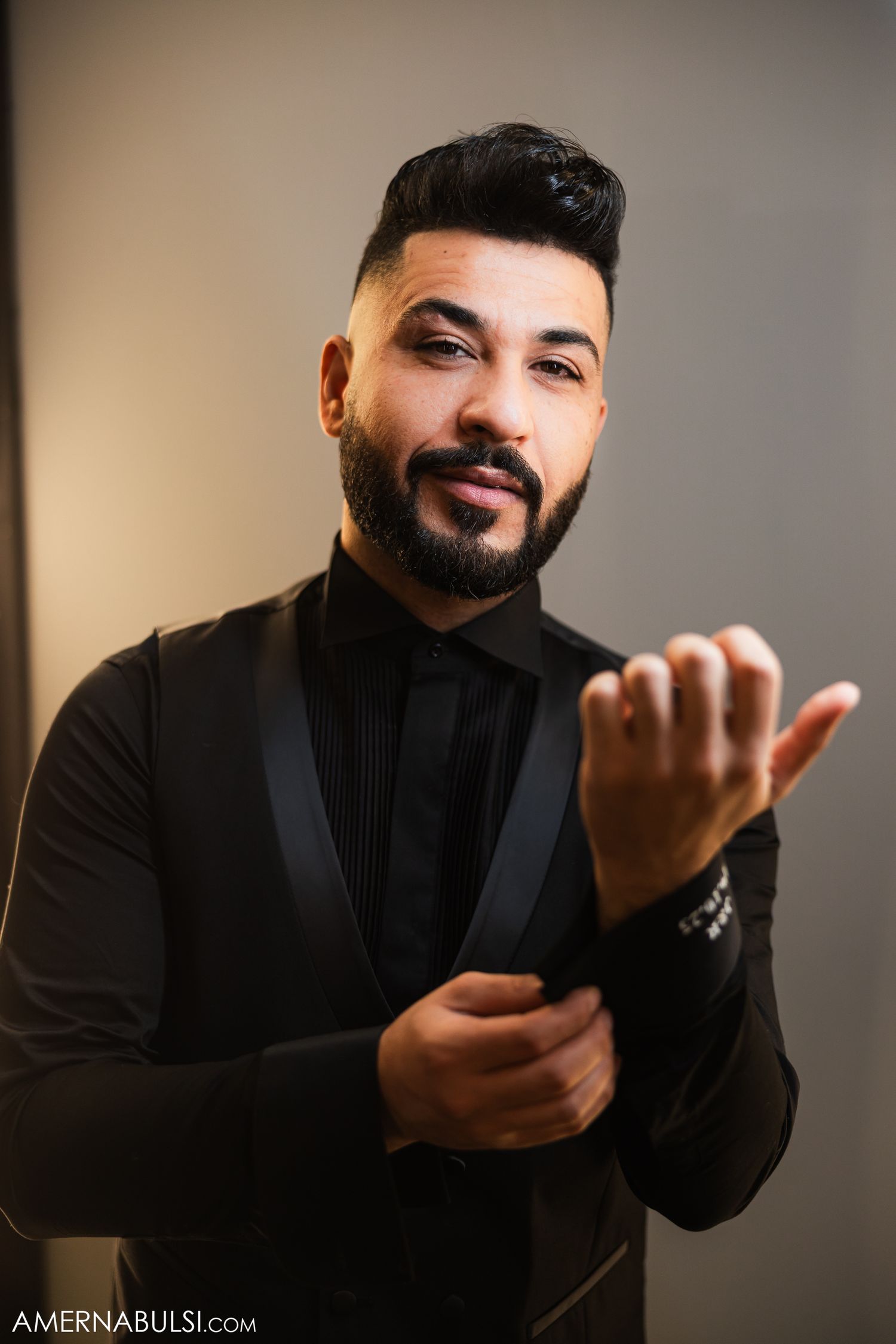 A person in a black turtleneck sweater gestures expressively while seated in a studio setting.