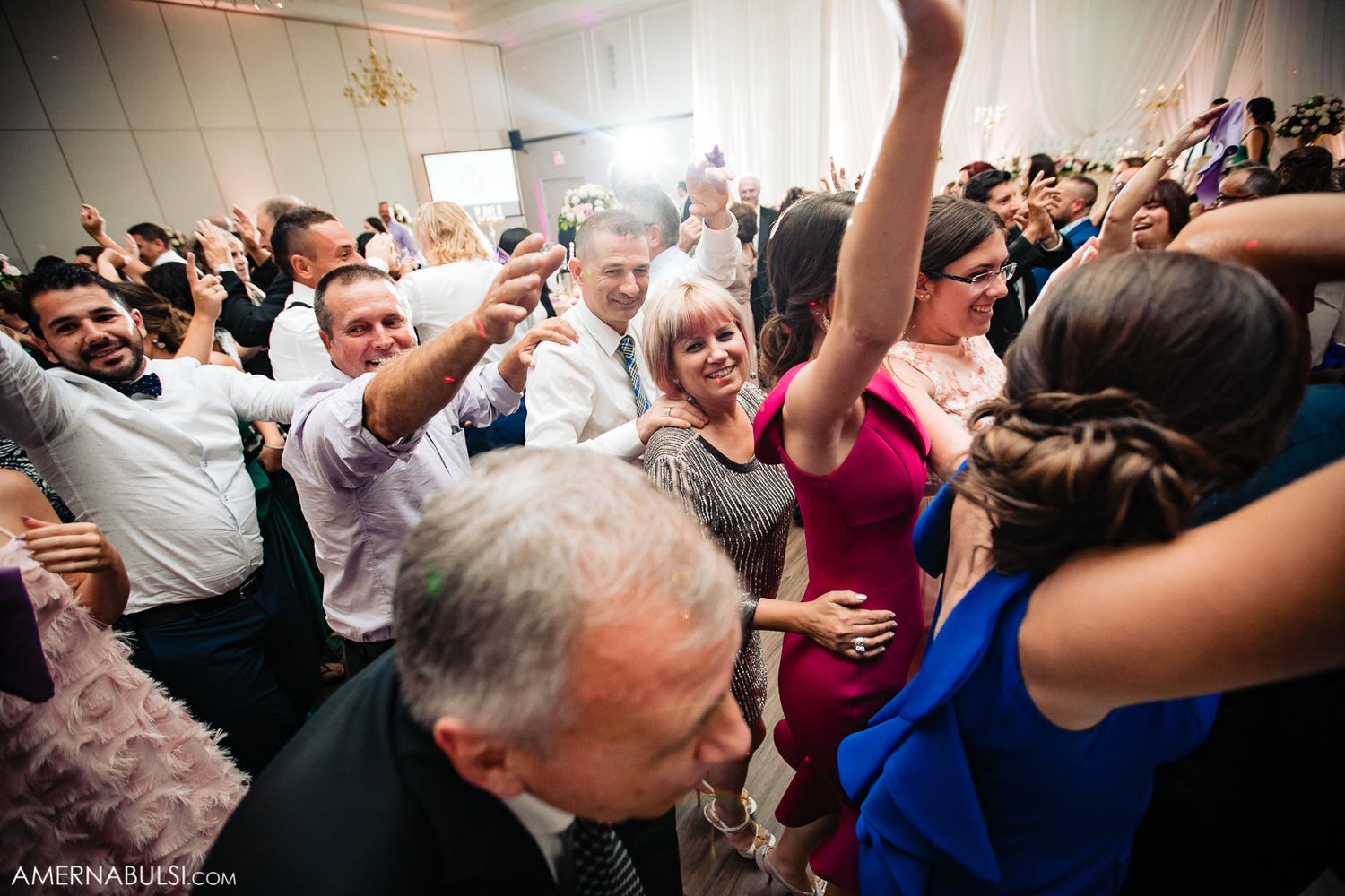 Wedding guests dancing and celebrating together in a lively reception hall filled with joyful energy.