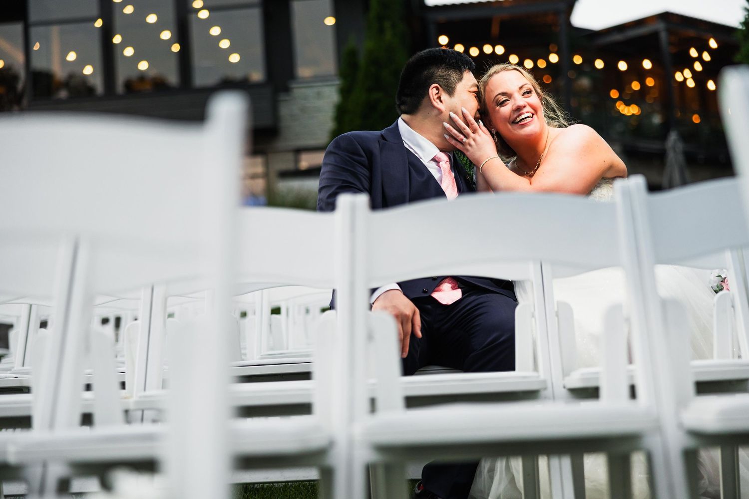 White wedding ceremony chairs arranged outdoors with string lights overhead.