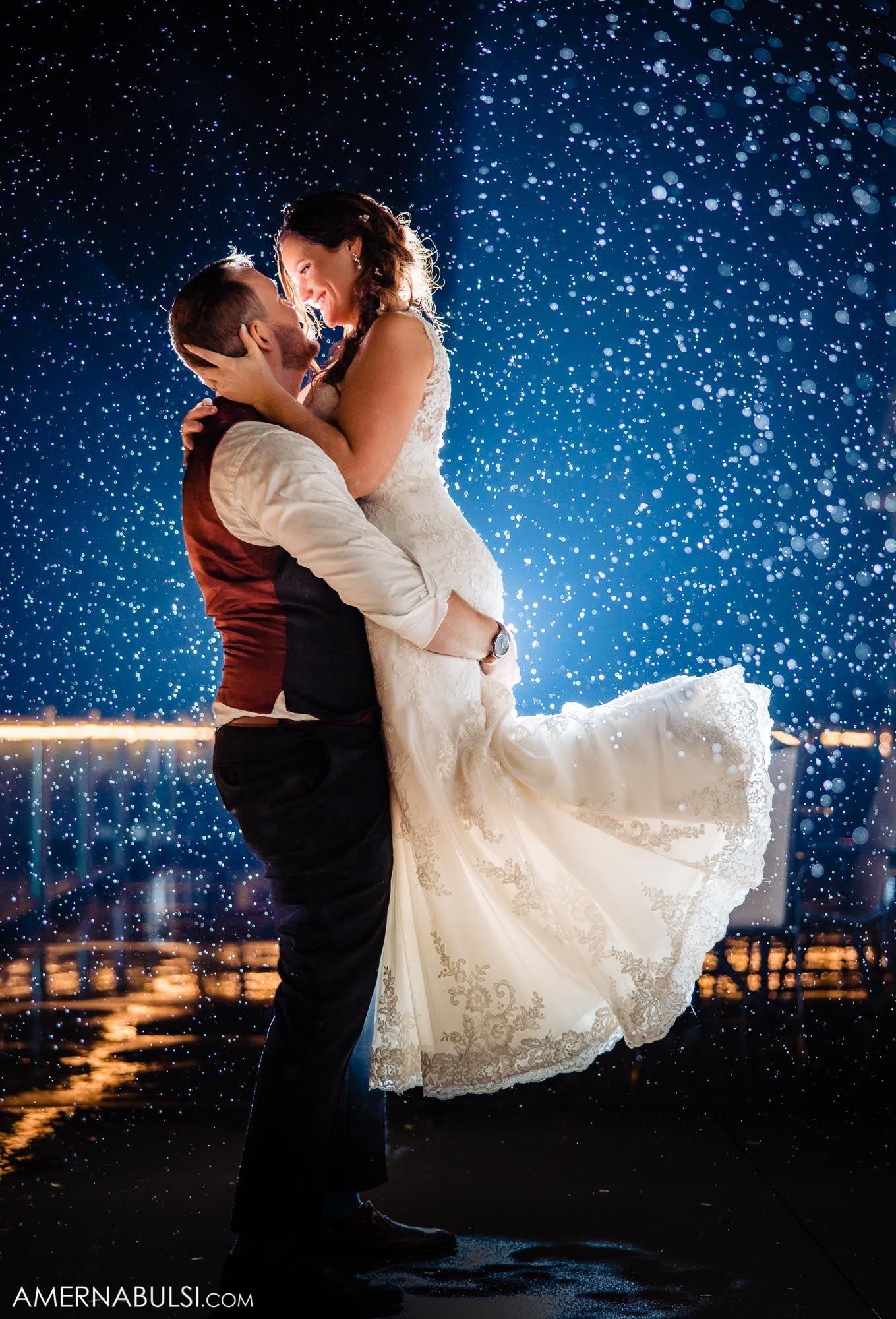 Romantic nighttime wedding portrait with couple dancing under starry sky and city lights.