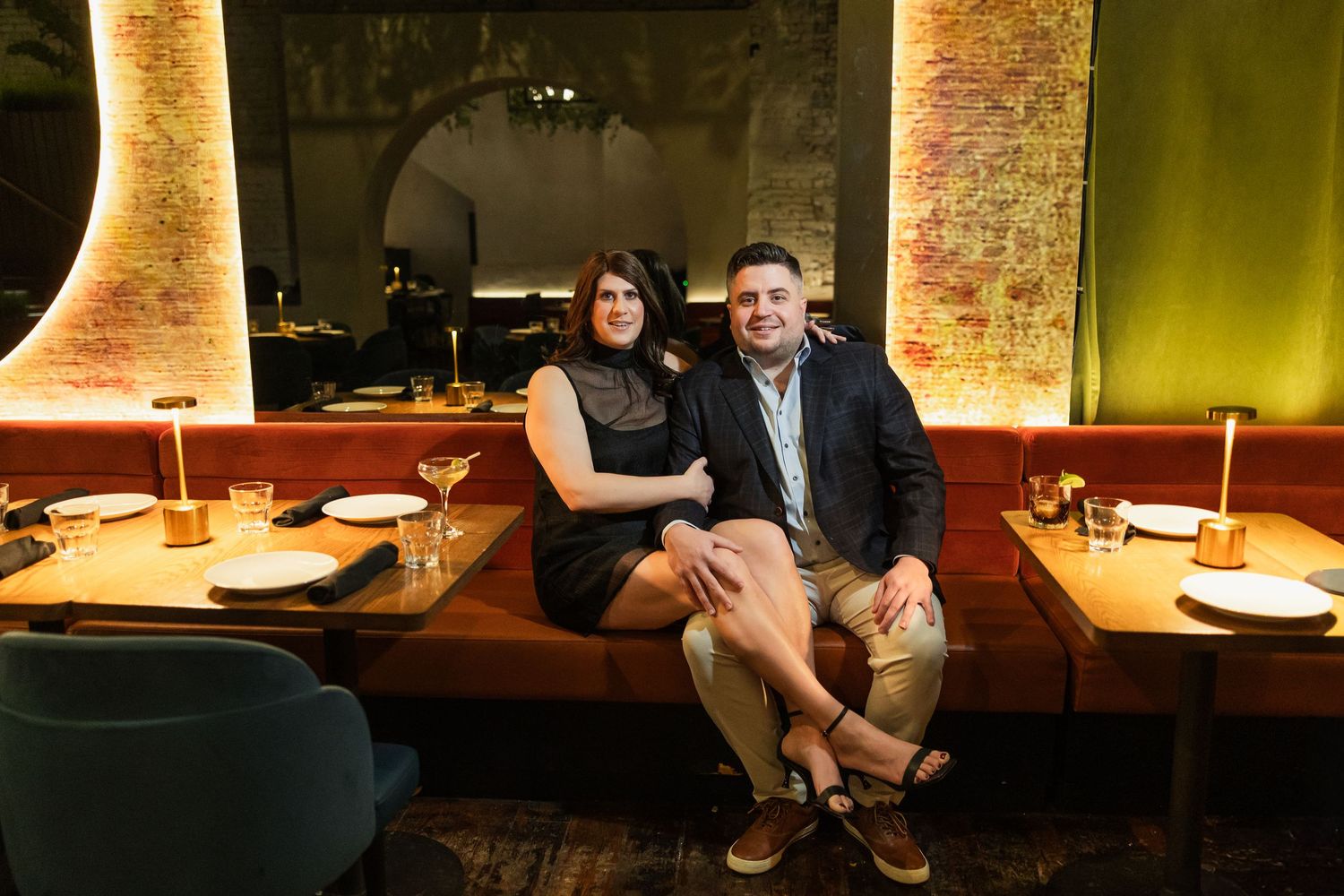 Couple smiling together on a red booth seat inside an elegant dimly lit restaurant with warm ambient lighting.