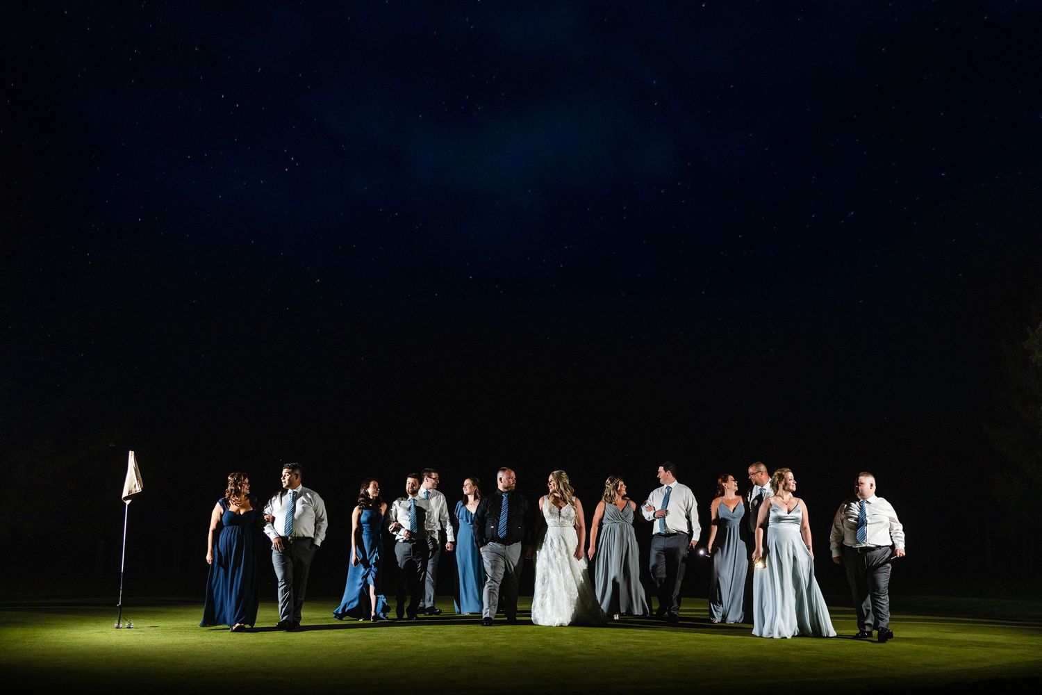 Wedding party silhouettes stand together at night under dramatic outdoor lighting.