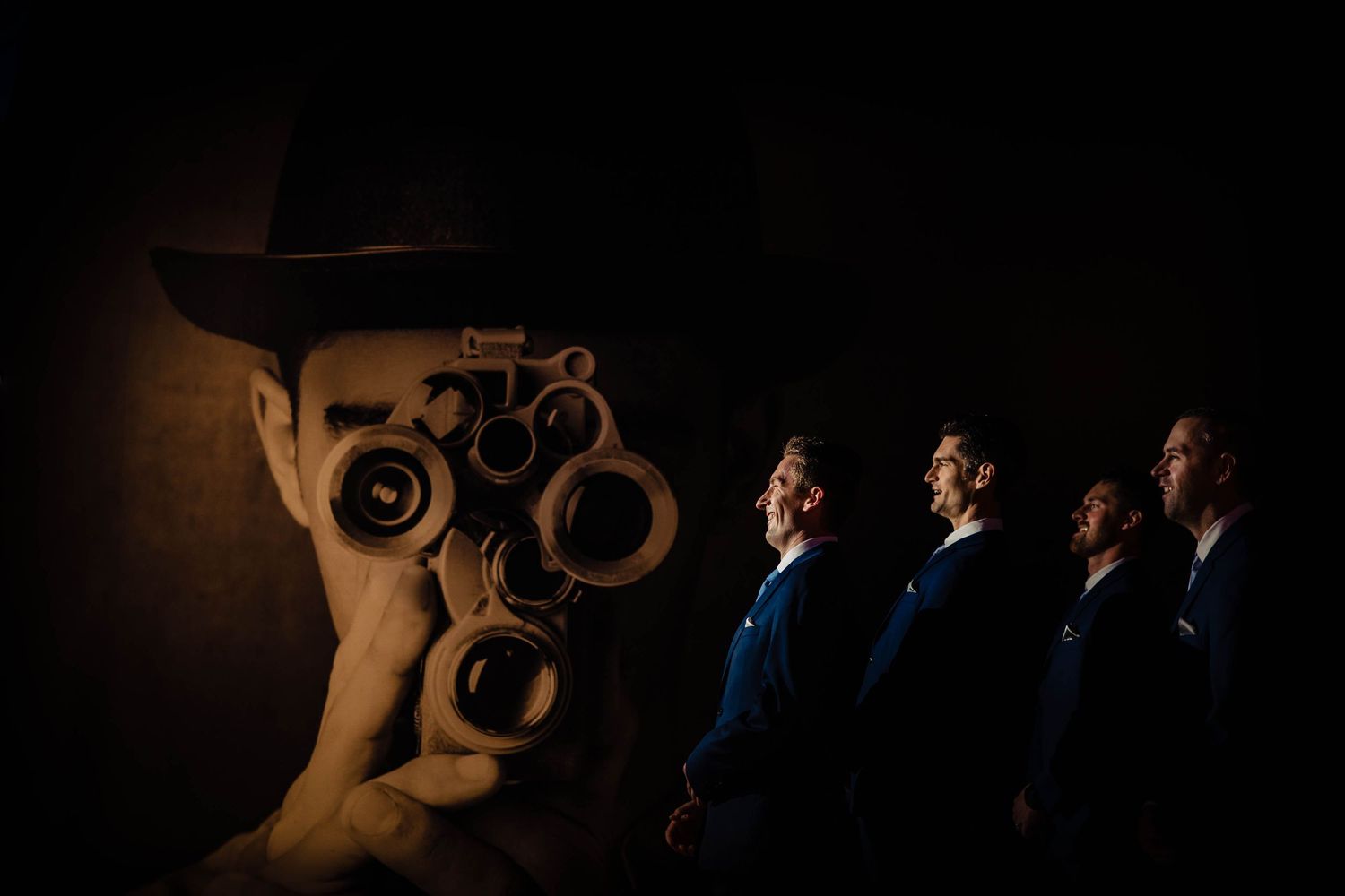 Stylized low-light portrait of groomsmen arranged in dramatic composition against dark background.