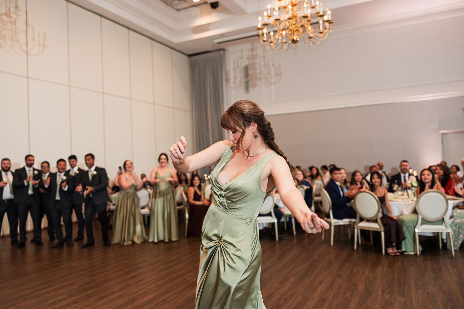 Woman in sage green gown dancing at elegant wedding reception with guests watching in background.