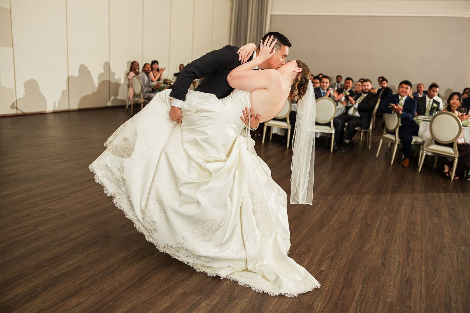 Groom dips bride for a romantic kiss during their first dance at an elegant wedding reception.