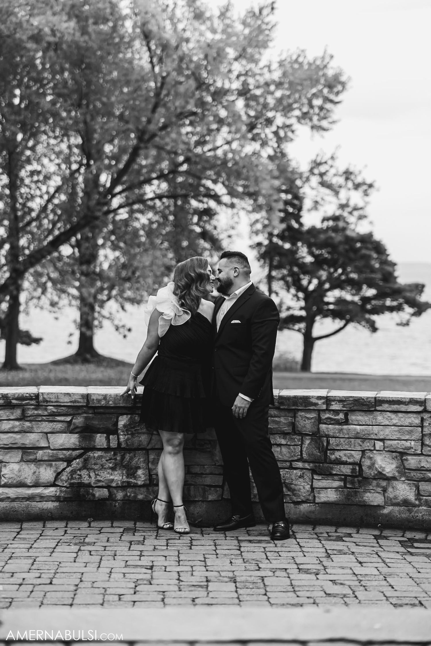 A romantic black and white photo of a couple by a stone wall.