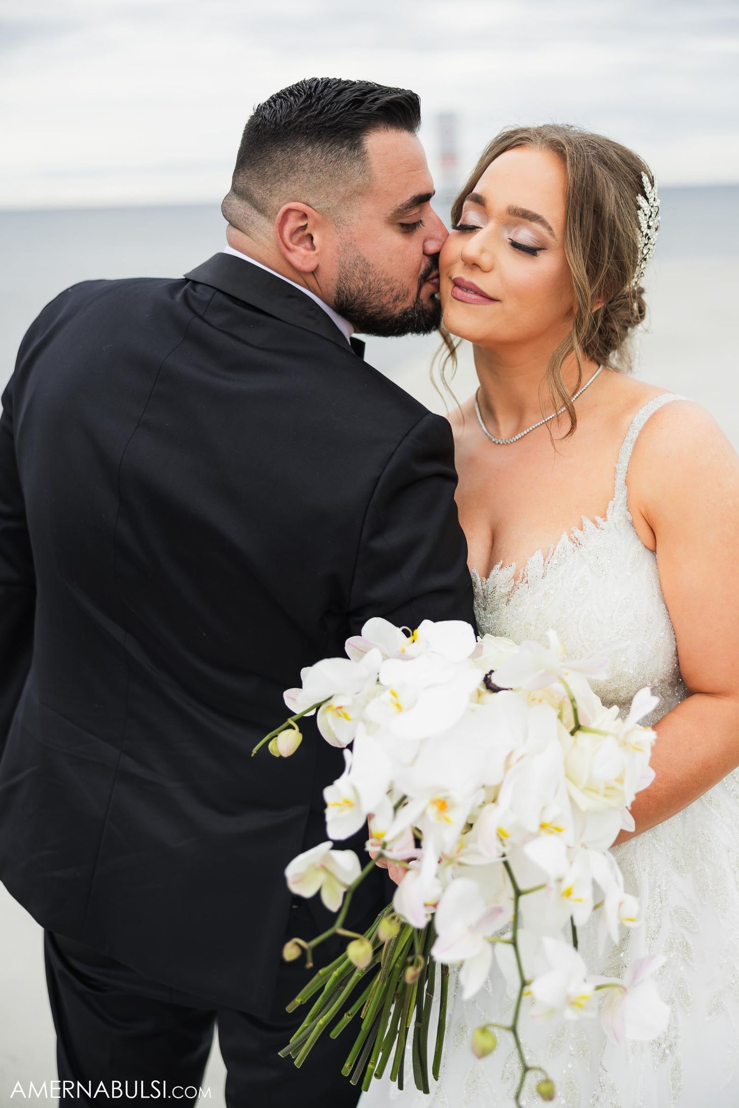 Romantic wedding portrait with white orchid bouquet against seaside backdrop.