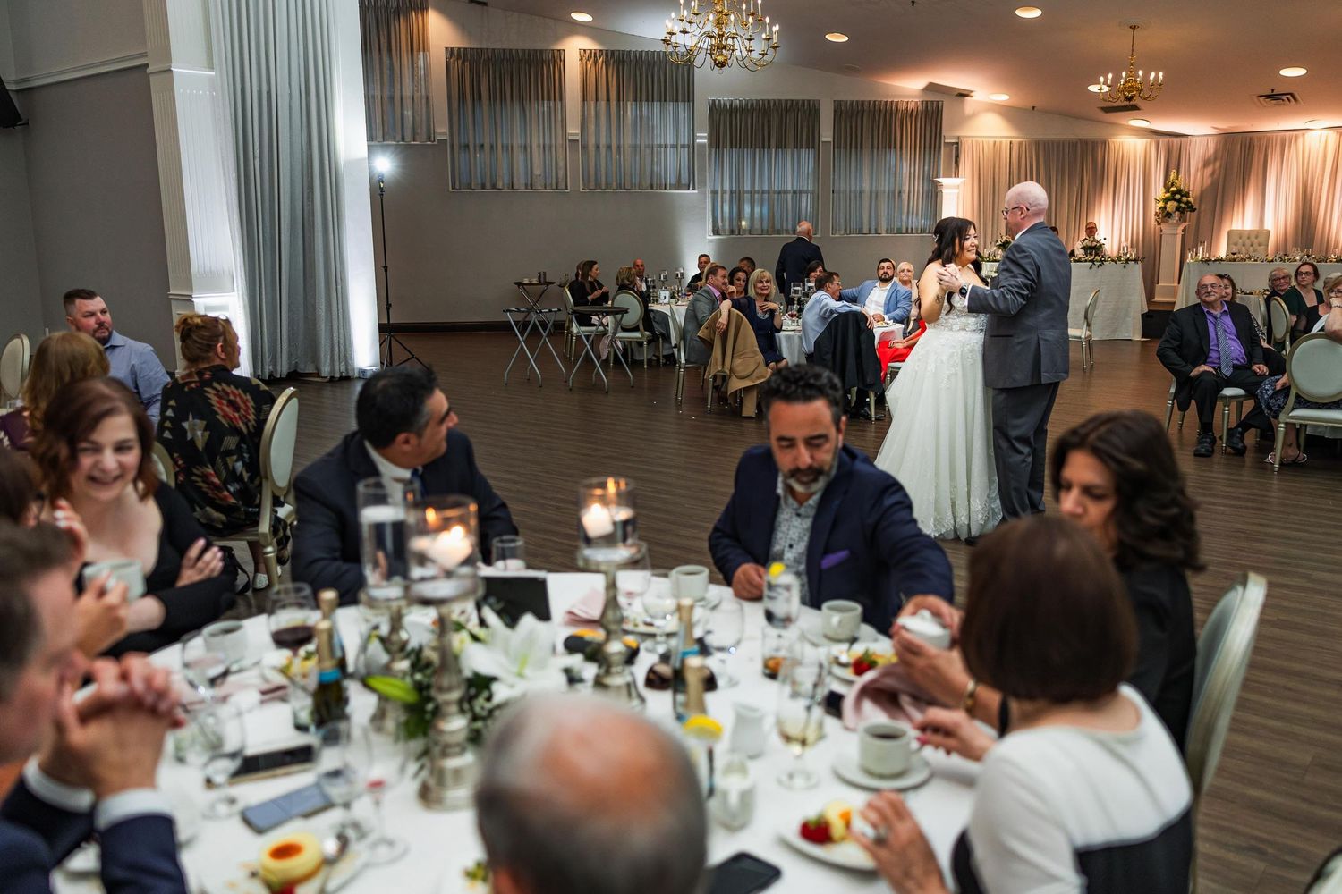 Wedding guests enjoying dinner at decorated round tables during an indoor reception.