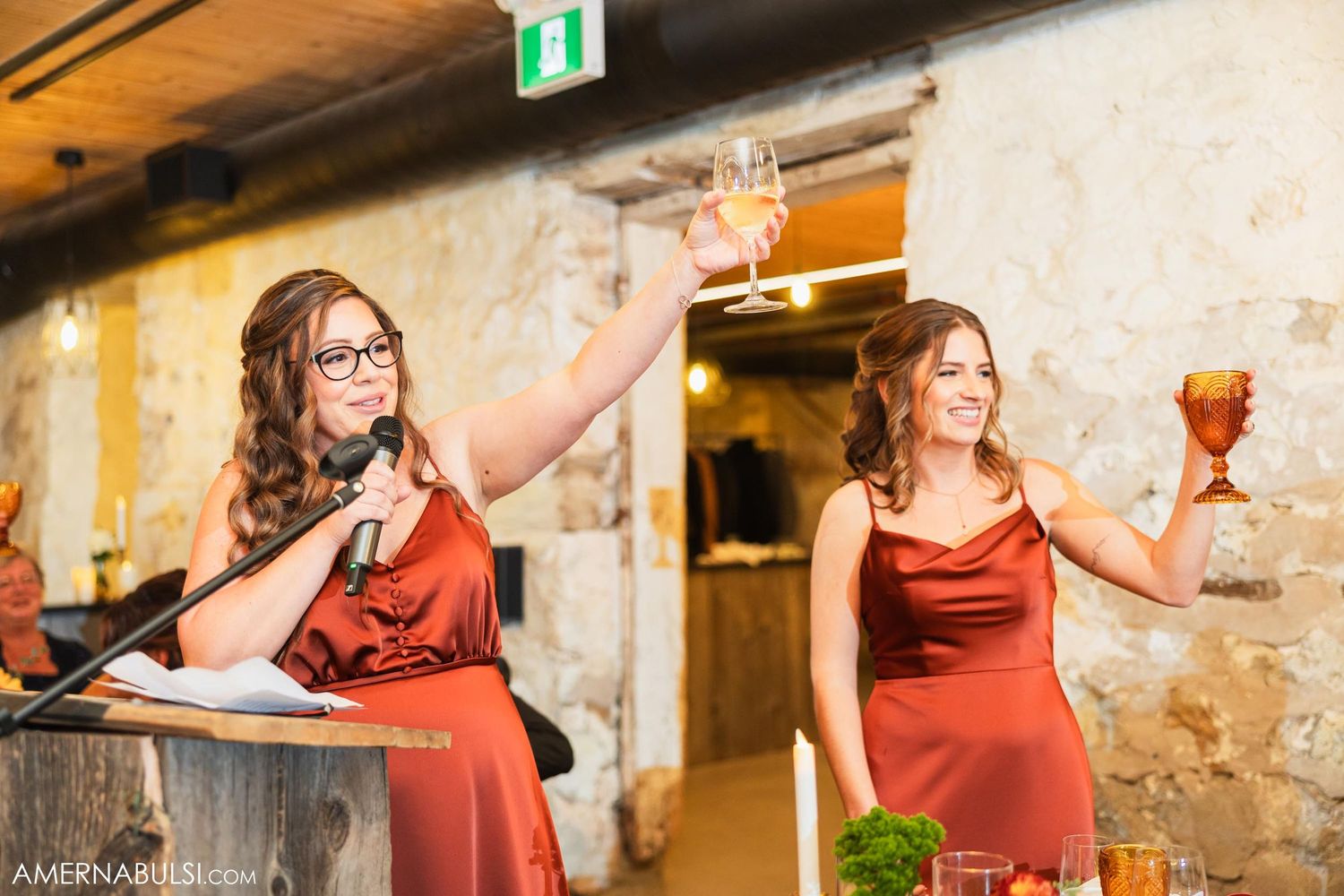 Two women in red dresses making a celebratory toast at an event.