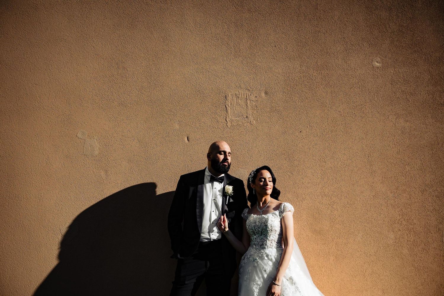 Artistic wedding portrait with dramatic shadows against textured wall.