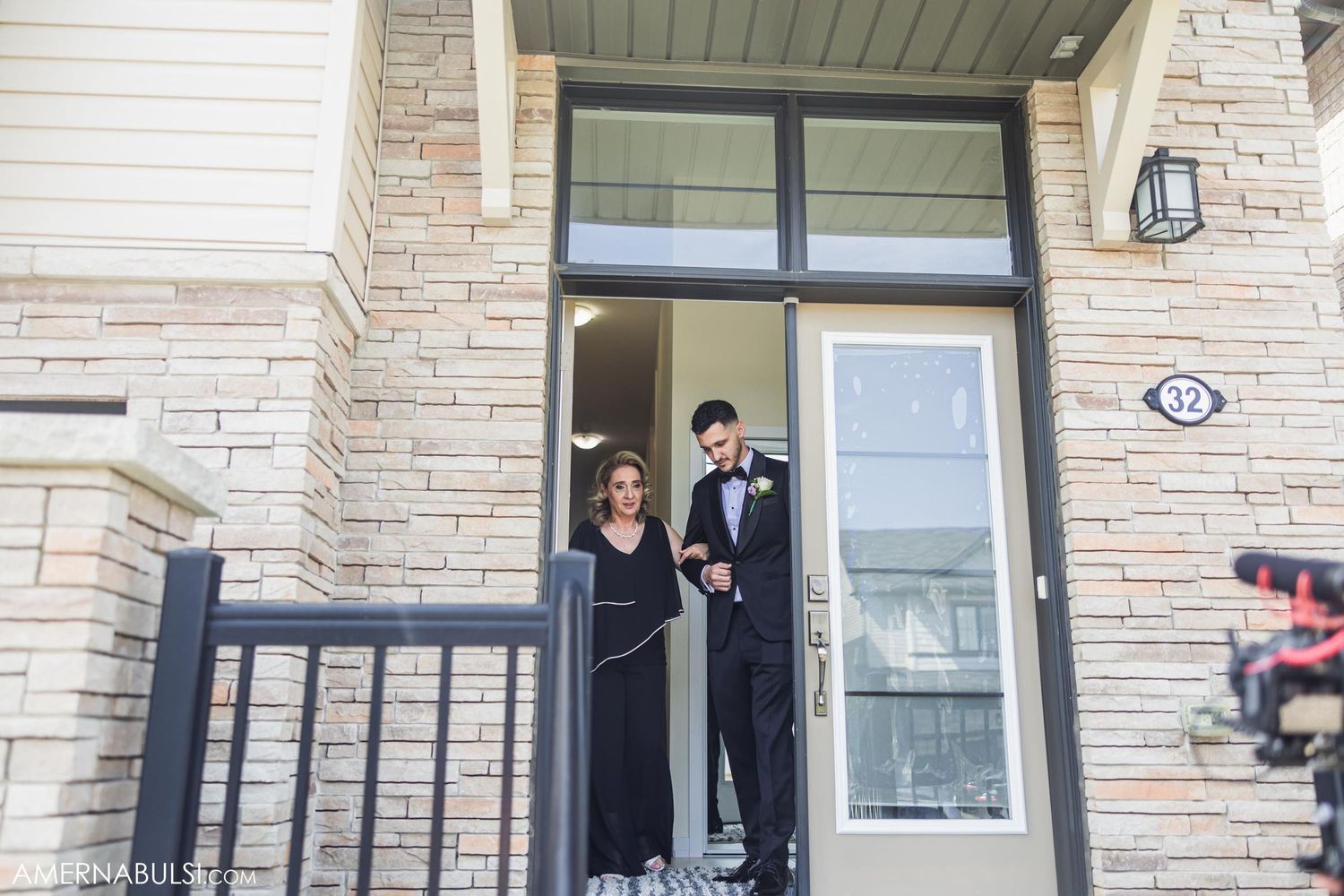 A couple standing in formal attire on their front porch steps.