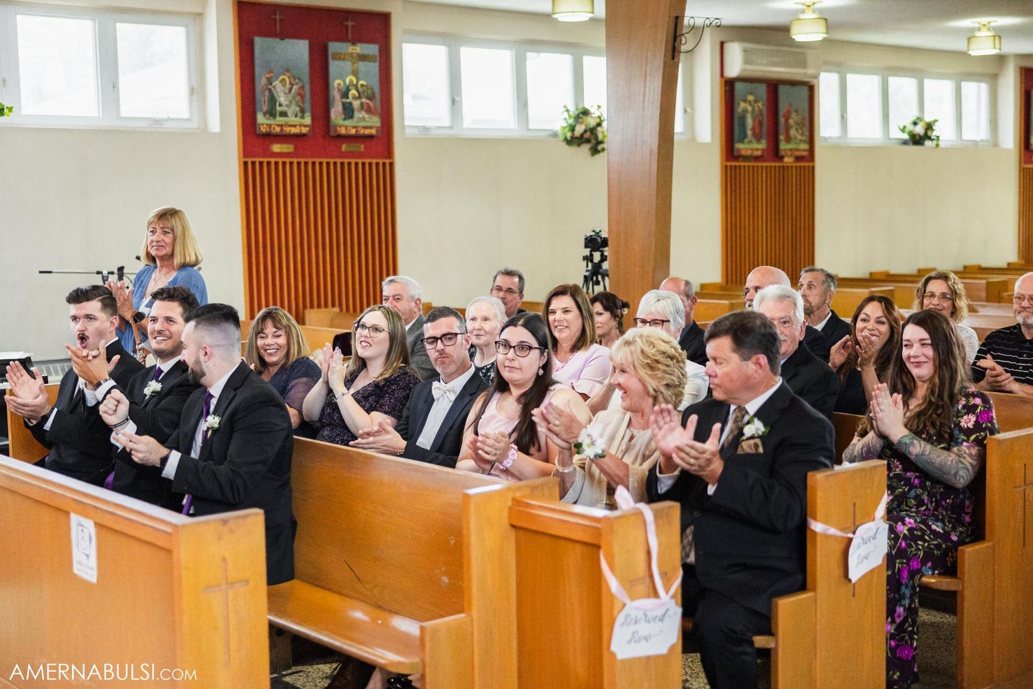 Wedding guests in church pews capture photos and celebrate during the ceremony.