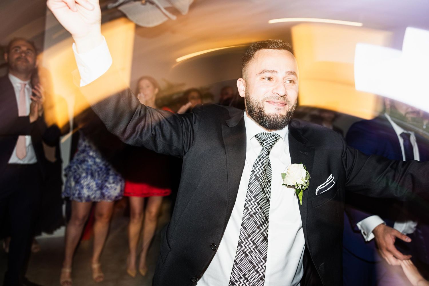A groomsman dances energetically on the wedding reception dance floor in a black suit and patterned tie.