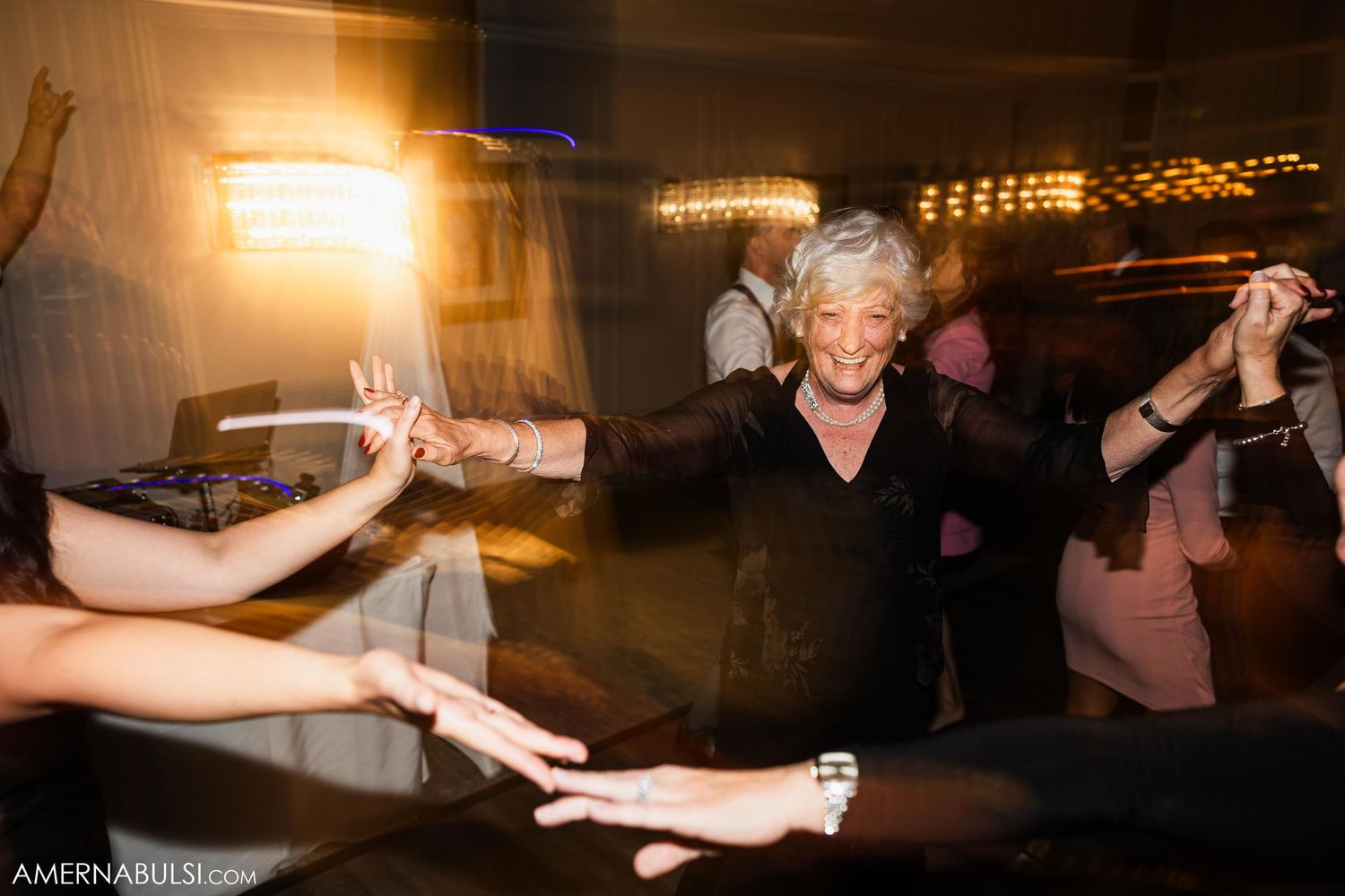 Wedding guests dance energetically on a dimly lit dance floor with motion blur effects and warm lighting.