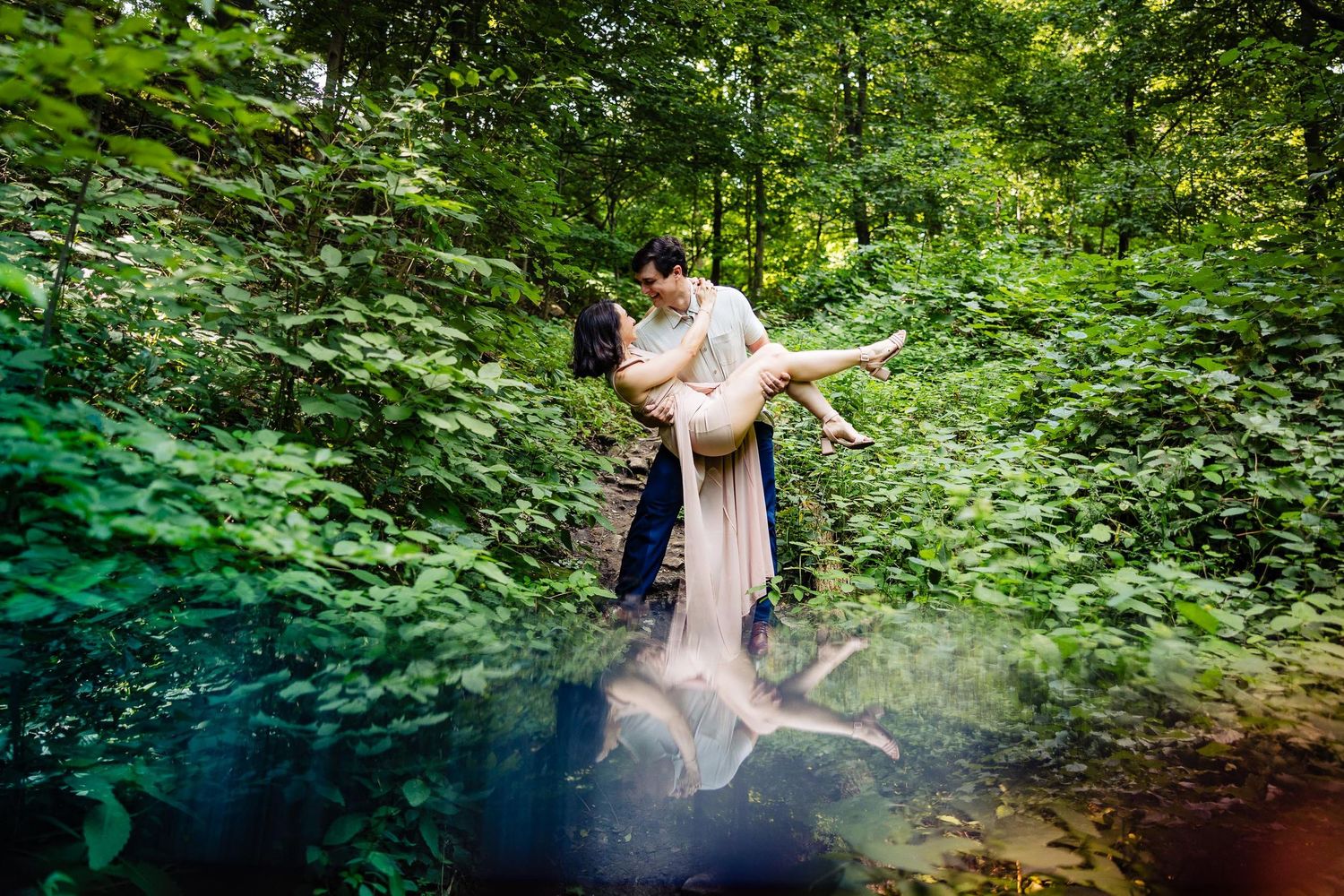 Romantic couple embrace by a misty pond surrounded by lush greenery.