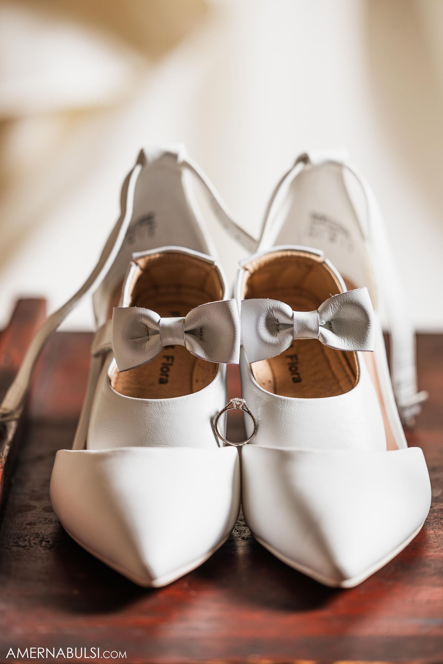 Elegant white wedding shoes with bow details on a wooden surface.