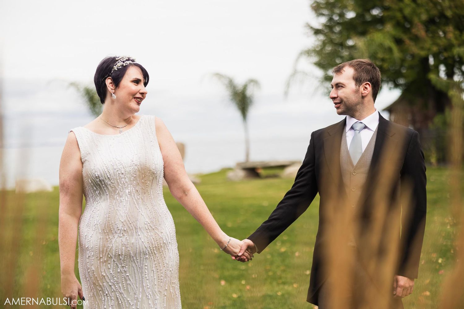 Joyful wedding couple sharing a candid moment on grassy oceanfront setting.