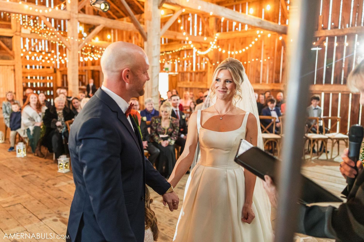 Candid moment during rustic barn wedding ceremony with string lights and wooden details.