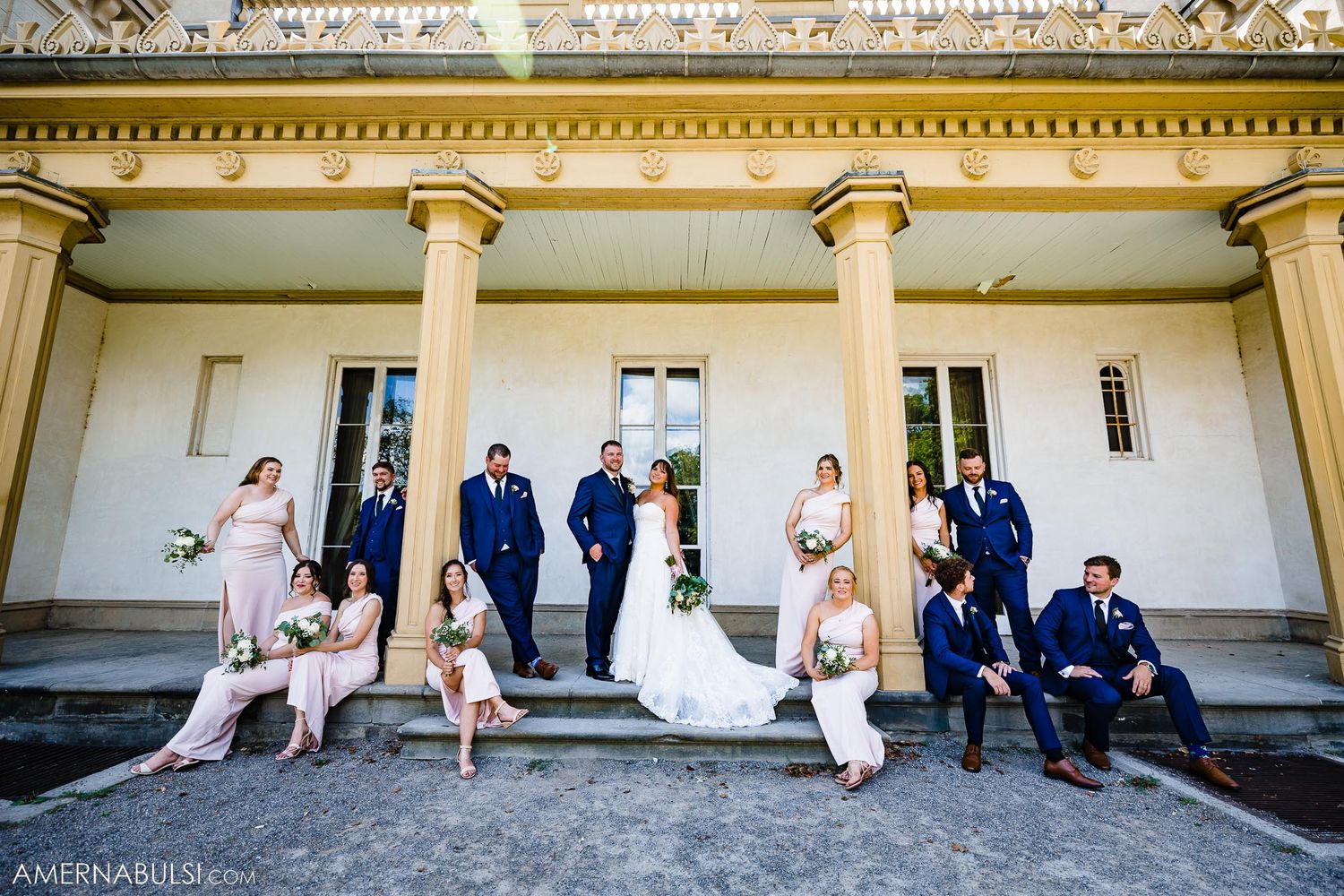 Wedding party positioned on grand white steps with classical columns in formal attire.