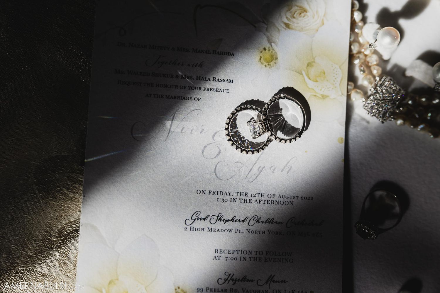 Artistic photo of wedding rings casting shadows on invitation paper.