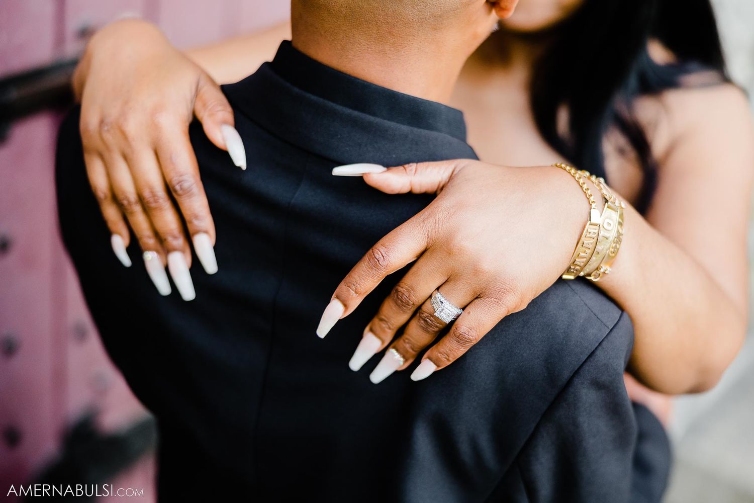 Close-up of hands wearing rings and jewelry against black formal attire.